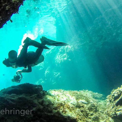 sidemount scooter diver exiting the cave with sunrays