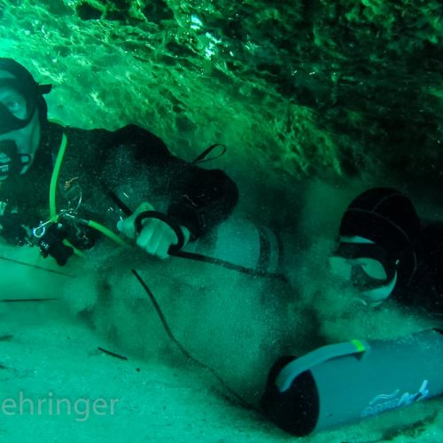 sidemount scooter divers passing a very small cave restriction